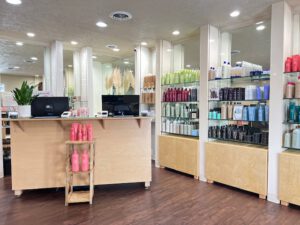 - Results Salon and Spa in Kingsport, TN A salon reception area with a wooden counter, point-of-sale terminals, and shelves displaying various hair care products in bottles. - Results Salon and Spa in Kingsport, TN