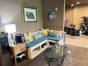- Results Salon and Spa in Kingsport, TN A waiting area with a blue cushioned corner bench, decorative pillows, a glass coffee table, wall art, and two black pedicure chairs in the background. - Results Salon and Spa in Kingsport, TN