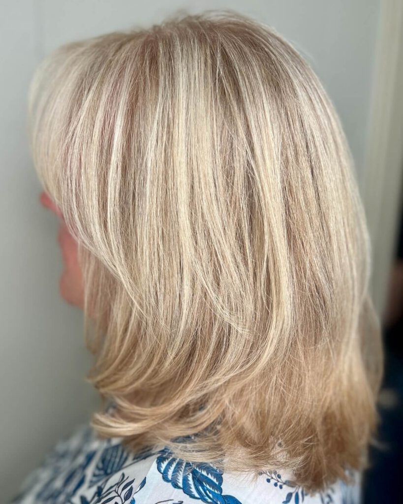 - Results Salon and Spa in Kingsport, TN Woman with shoulder-length, layered, straight blonde hair, shown from a side angle, wearing a white top with blue floral patterns. - Results Salon and Spa in Kingsport, TN