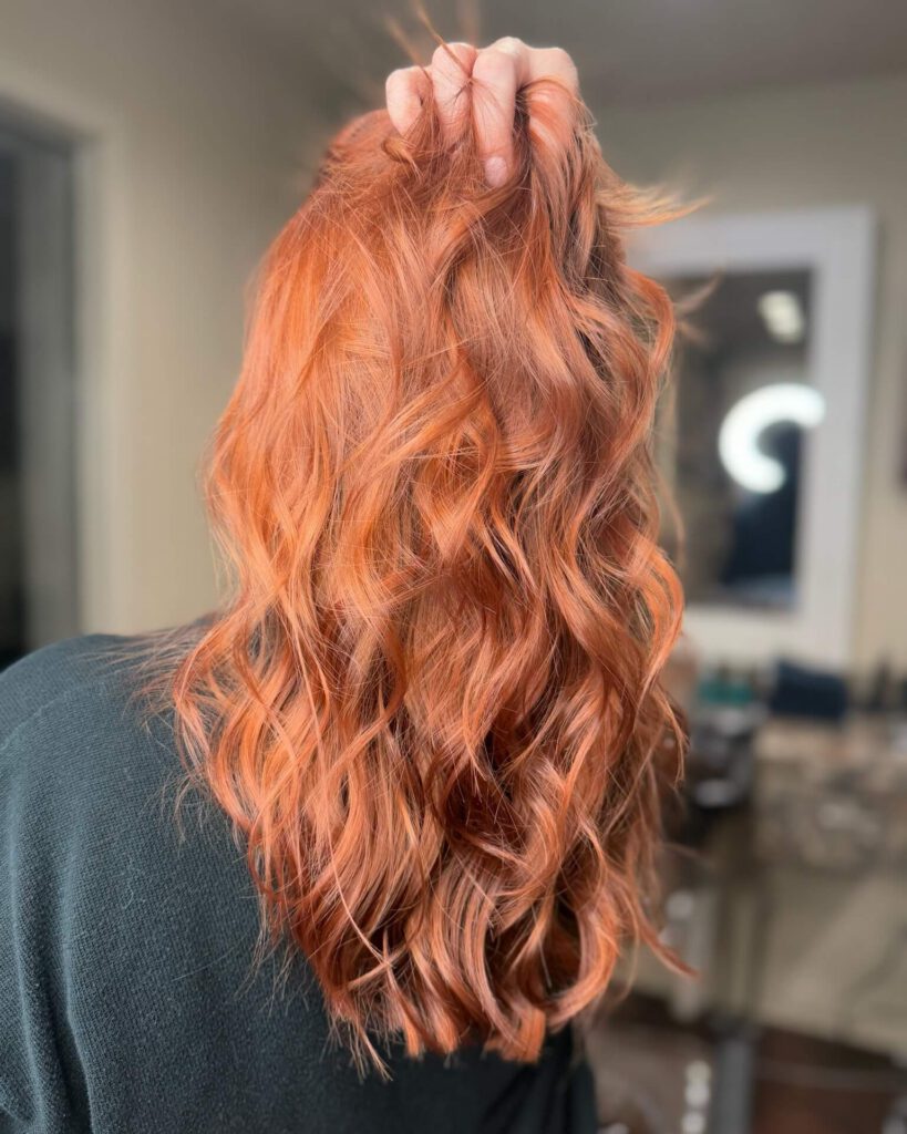 - Results Salon and Spa in Kingsport, TN Person with long, wavy, copper-colored hair holds up a section to show the texture and color. The background appears to be a salon. - Results Salon and Spa in Kingsport, TN