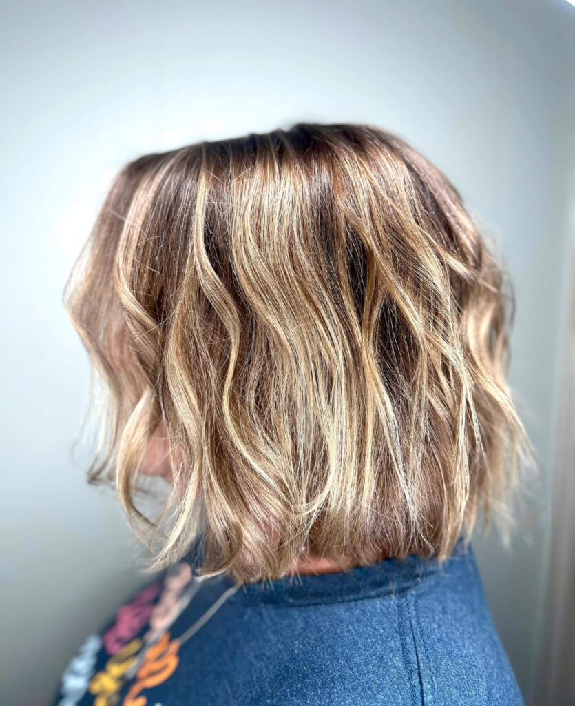 - Results Salon and Spa in Kingsport, TN A person with shoulder-length, wavy, blonde-highlighted hair is shown from the side against a plain background. - Results Salon and Spa in Kingsport, TN
